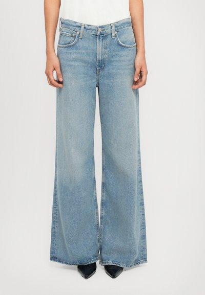 Jean large bleu clair avec taille haute, design classique à cinq poches et texture légèrement délavée. Associé à des talons aiguille noirs.