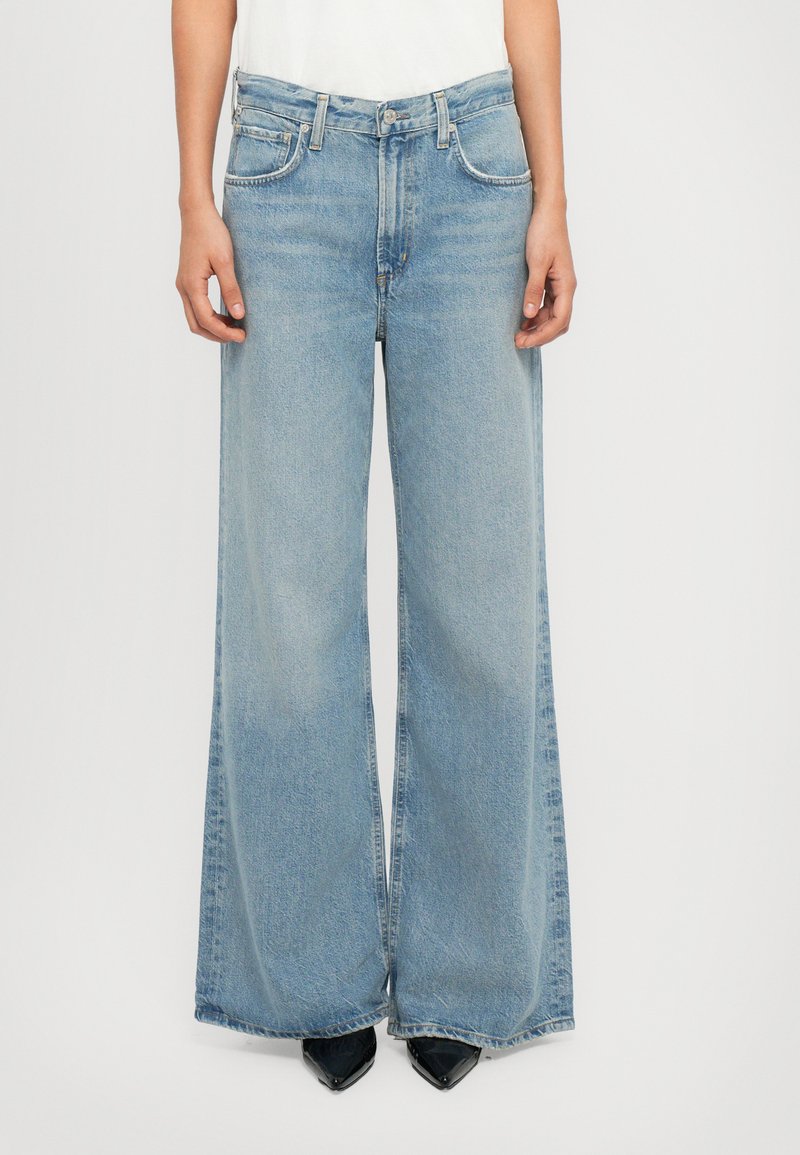 Jean large bleu clair avec taille haute, design classique à cinq poches et texture légèrement délavée. Associé à des talons aiguille noirs.