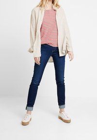 Leinenbeige Hemd über einem rot-weißen gestreiften T-Shirt, kombiniert mit dunkelblauen Skinny-Jeans und weißen Schuhen mit Jutsohle.