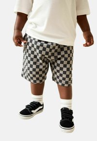 Schwarz-graue karierte Shorts mit elastischem Bund; kombiniert mit schwarzen und weißen Klettverschluss-Sneakern und weißen Sneakersocken.