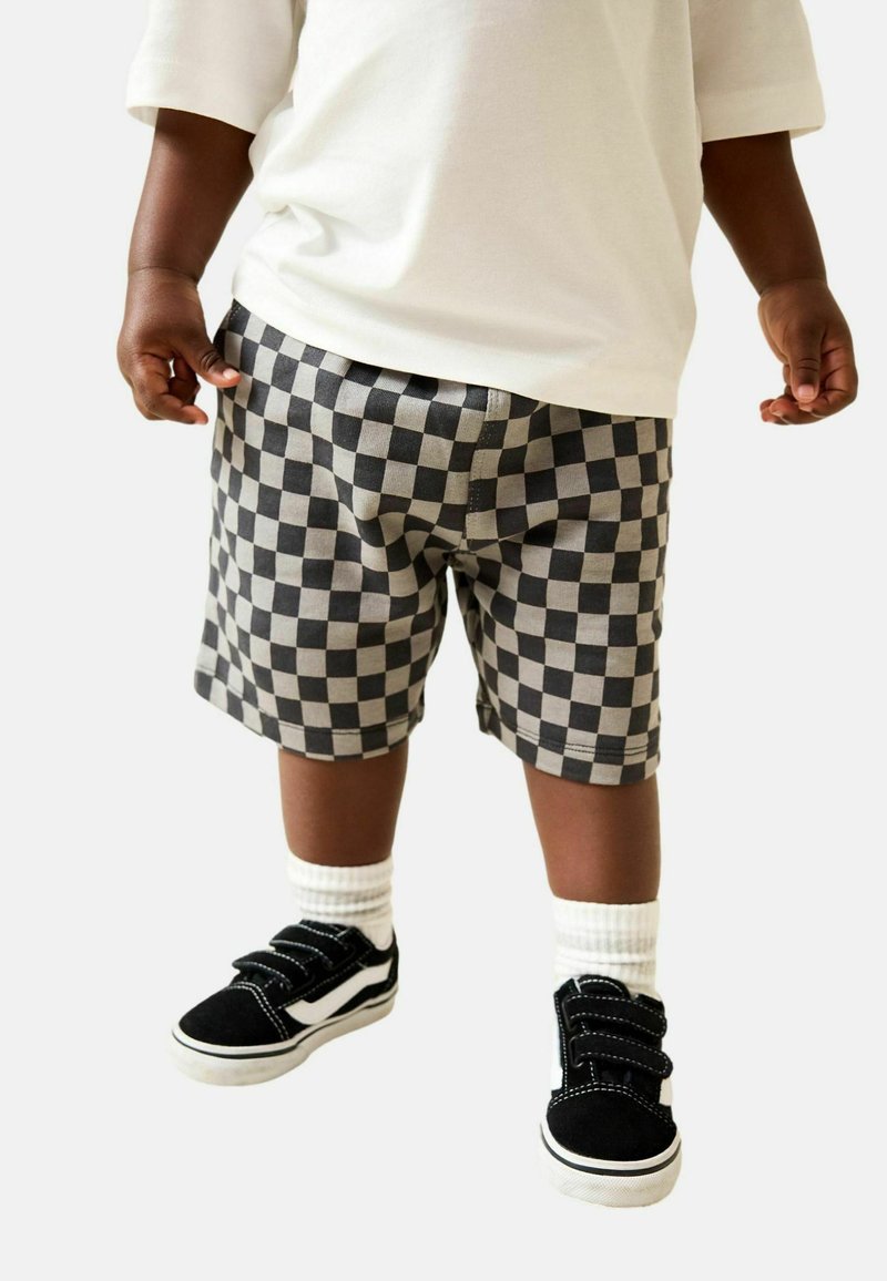 Schwarz-graue karierte Shorts mit elastischem Bund; kombiniert mit schwarzen und weißen Klettverschluss-Sneakern und weißen Sneakersocken.