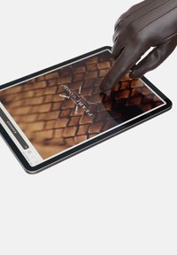 Smeđa kožna rukavica sa detaljima na šavovima dodiruje tablet koji prikazuje teksturiranu pozadinu u toplim tonovima i logotip u sredini.
