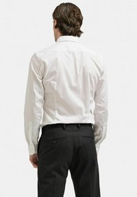 Vit långärmad skjorta med spetsig krage. Slät tyg, knäppta manschettdetaljer, bärs med svarta byxor som har två bakfickor.