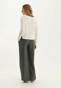 Pull en maille côtelé crème avec col rond, associé à un pantalon large vert olive. Maille texturée et coupe décontractée, idéal pour un look décontracté.