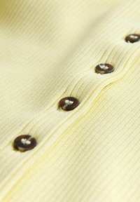 Gros plan sur un tissu jaune à nervures avec quatre boutons marron cousus en ligne verticale.