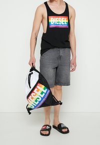 Svart linne med en regnbågsfärgad "DIESEL"-logga, grå shorts, en svart och vit dragsko-väska samt svarta sandaler med logga.