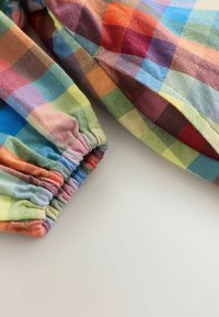 Färgglad rutigt tyg med en blandning av röda, blå, gröna och gula rutor. Elastiska muddarna ger en samlad textur.