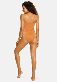 Pomarańczowy jednoczęściowy kostium kąpielowy z marszczeniami, regulowane krzyżujące się ramiączka i fakturowany, połyskujący materiał. Posiada umiarkowane zakrycie pleców.