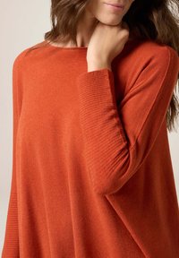 Locker sitzender oranger Pullover mit rundem Ausschnitt und gerippten Bündchen. Weicher Stoff mit einem leichten Glanz und glatter Körperware.
