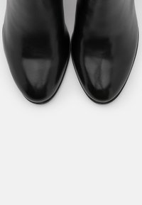 Botines de cuero negro de diseño elegante, con punta afilada y textura suave. La suela es plana con acentos mínimos, enfatizando una apariencia pulida.