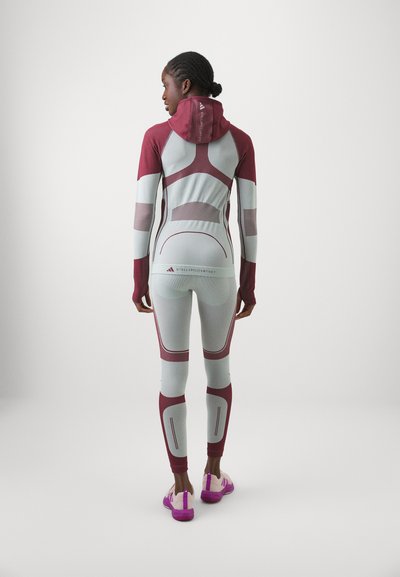 Világosszürke sportos együttes bordó akcentusokkal. Formához simuló kialakítás, texturált panelek és kapucni jellemzi. Rózsaszín és lila lábbeli.