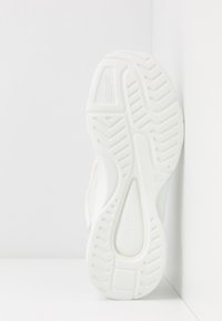 Semelle de basket blanche à texture rainurée, présentant une tige en caoutchouc lisse et des accents latéraux gris et rose pâle. Design durable et léger.