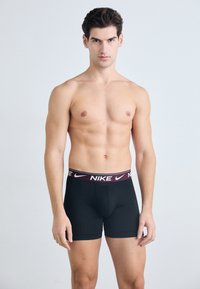 Crne bokserice s bordo elastičnim pojasom na kojem piše "NIKE" bijelim slovima. Glatka tkanina s uskim fitom i podržavajućim dizajnom džepa.