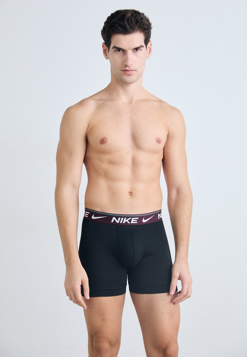 Crne bokserice s bordo elastičnim pojasom na kojem piše "NIKE" bijelim slovima. Glatka tkanina s uskim fitom i podržavajućim dizajnom džepa.