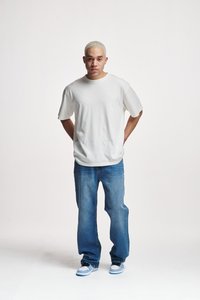 Hvit oversized t-skjorte, løs passform, kombinert med blå straight-leg jeans og lyseblå sneakers, stående mot en ensfarget bakgrunn.
