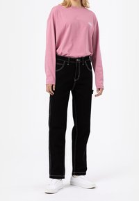 Long-sleeve pink t-shirt with a round neckline and white logo, paired with black pants featuring white stitching and a straight-leg cut.