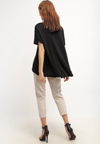 Top nero, dalla vestibilità ampia e con maniche corte, abbinato a pantaloni tapered color crema e decolleté neri con cinturino alla caviglia. Tessuto dalla texture liscia.