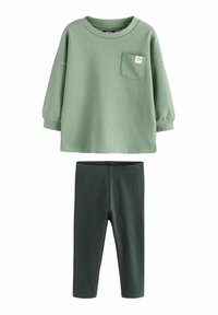 Grüner Baumwollpullover mit einer Tasche und Sternenmotiv, kombiniert mit dunkelgrünen Rippleggings. Weicher Stoff, lockere Passform und lange Ärmel.