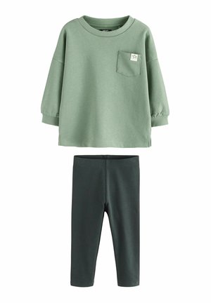 Grüner Baumwollpullover mit einer Tasche und Sternenmotiv, kombiniert mit dunkelgrünen Rippleggings. Weicher Stoff, lockere Passform und lange Ärmel.