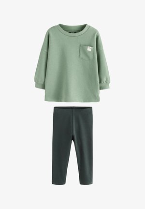 Zielony bawełniany sweter z kieszenią i detalem w kształcie gwiazdy, w zestawie z ciemnozielonymi prążkowanymi legginsami. Miękka tekstura, luźny krój i długie rękawy.