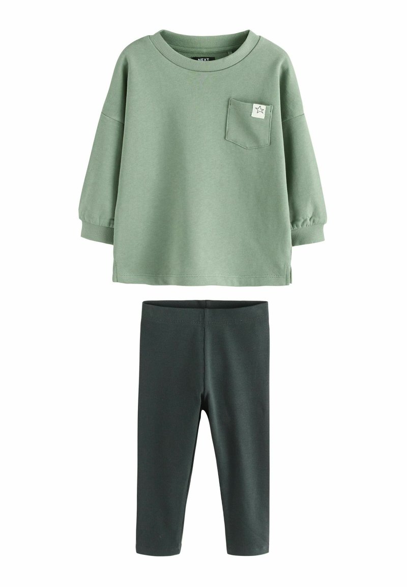 Suéter de algodón verde con un bolsillo y detalle de estrella, combinado con leggings acanalados verdes oscuros. Textura suave, corte relajado y mangas largas.