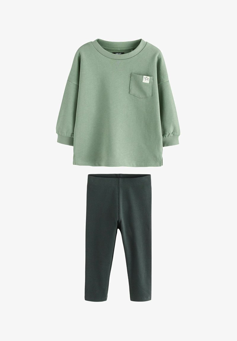 Grüner Baumwollpullover mit einer Tasche und Sternenmotiv, kombiniert mit dunkelgrünen Rippleggings. Weicher Stoff, lockere Passform und lange Ärmel.