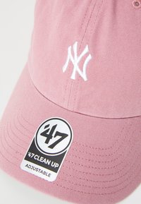Cappellino da baseball regolabile rosa con logo "NY" ricamato bianco, tessuto texturizzato e un'etichetta nera con la scritta "47 Clean Up."