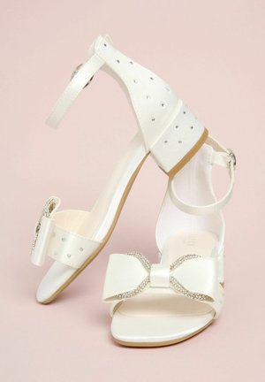 Hvide blokhøje sko med åben tå og ankelremme, pyntet med sløjfer med rhinsten og små rhinsten på hælen og remmen.
