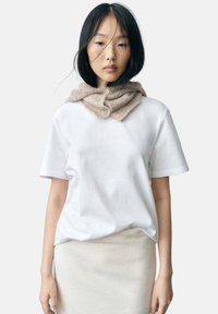 Vit bomull T-shirt med korta ärmar och en avslappnad passform, ihop med en ljusbeige scarf i mjukt stickat material runt halsen.