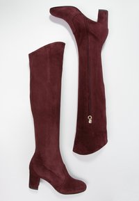 Botas de ante burdeos hasta la rodilla con tacón ancho, cremallera lateral y textura suave; el caño presenta un diseño contorneado para un mejor ajuste.