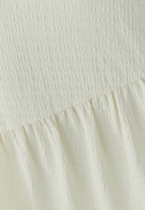 Cremfarbener Stoff mit geraffter Textur und einem gerafften, elastischen oberen Abschnitt, der in einen locker fallenden unteren Abschnitt übergeht.