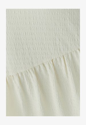 Tessuto color crema con texture arricciata e una parte superiore arricciata ed elastica che si trasforma in una parte inferiore che scorre liberamente.