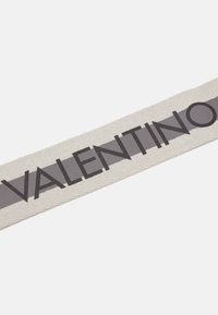 Ruban en tissu beige avec une bande gris foncé et "VALENTINO" imprimé en lettres grasses, présentant une surface texturée et des bords droits.