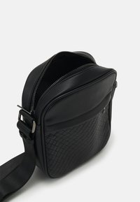 Black crossbody bag made of smooth leather with a woven texture on the front, featuring a zip closure and adjustable strap.
