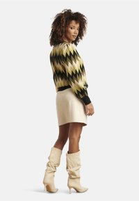 Wavy-patterned sweater in black, olive, and gold paired with a cream mini skirt and beige slouchy high-heeled boots.
