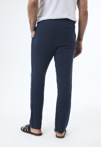 Navy blue trousers made of lightweight fabric, featuring side pockets, back pockets, and a straight-leg design. Worn with black sandals.