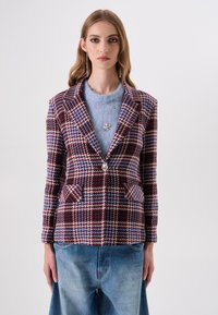 Geruit colbert in bordeauxrood, blauw en cr�èmekleurig. Opvallende details zijn onder andere een enkele knoopsluiting en twee zakken aan de voorkant. Draagt over een blauwe top.