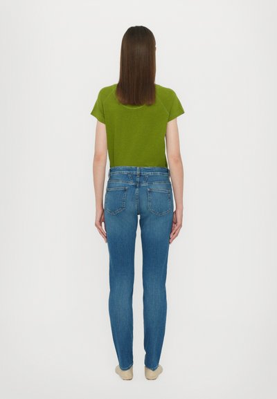 Grønn kortermet topp og blå skinny jeans, sett fra baksiden. Jeansene har baklommer og et liv. Glatt stoffstruktur.