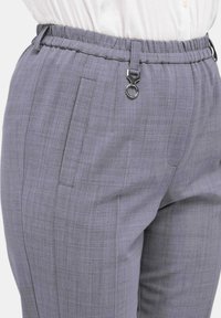 Grijze stoffen broek met een gestructureerd patroon, voorzien van een gegolfde elastische tailleband, zijzakken en een ronde metalen accent.