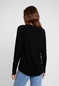 Pull noir à manches longues en matière douce avec un col rond et des manches raglan, doté d'un ourlet arrondi et d'une texture minimale.
