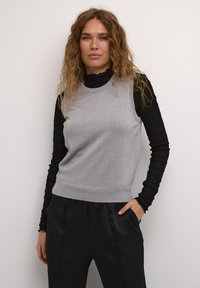 Pilka be rankovių palaidinė su tekstūruotu paviršiumi, dėvima virš juodos ilgomis rankovėmis palaidinės. Turi apvalų kaklą ir prigludusį dizainą.