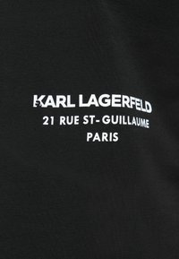 Černá látka s bílým textem "KARL LAGERFELD 21 RUE ST-GUILLAUME PARIS" psaným tučně a velkými písmeny.