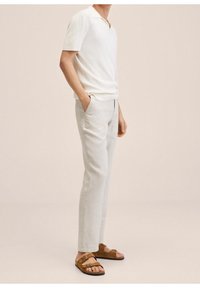 Biała koszulka polo z krótkim rękawem, jasnoszare spodnie, brązowe zamszowe sandały z podwójnymi paskami i klamrą, minimalistyczny design i miękkie tekstury.