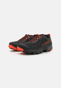 Schwarze Trailrunning-Schuhe mit orangen Akzenten, ausgestattet mit einem Obermaterial aus Mesh, einer aggressiven Außensohle und kontrastierenden Schnürsenkeln für einen sicheren Sitz.