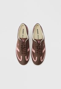 Ζευγάρι καφέ και ροζ αθλητικών παπουτσιών HUGO με κορδόνια, φωτογραφημένα από πάνω σε απλό λευκό φόντο.