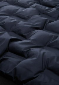 Dunkelblaues, geometrisch gequiltetes Material mit einer weichen Textur, das erhöhte, einheitliche Quadrate aufweist und einen gepolsterten Effekt über die gesamte Oberfläche erzeugt.