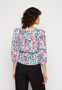 Blusa floral com mangas curtas e franzidas, apresentando padrões florais em rosa e azul sobre um fundo branco, cintura ajustada e tecido leve.