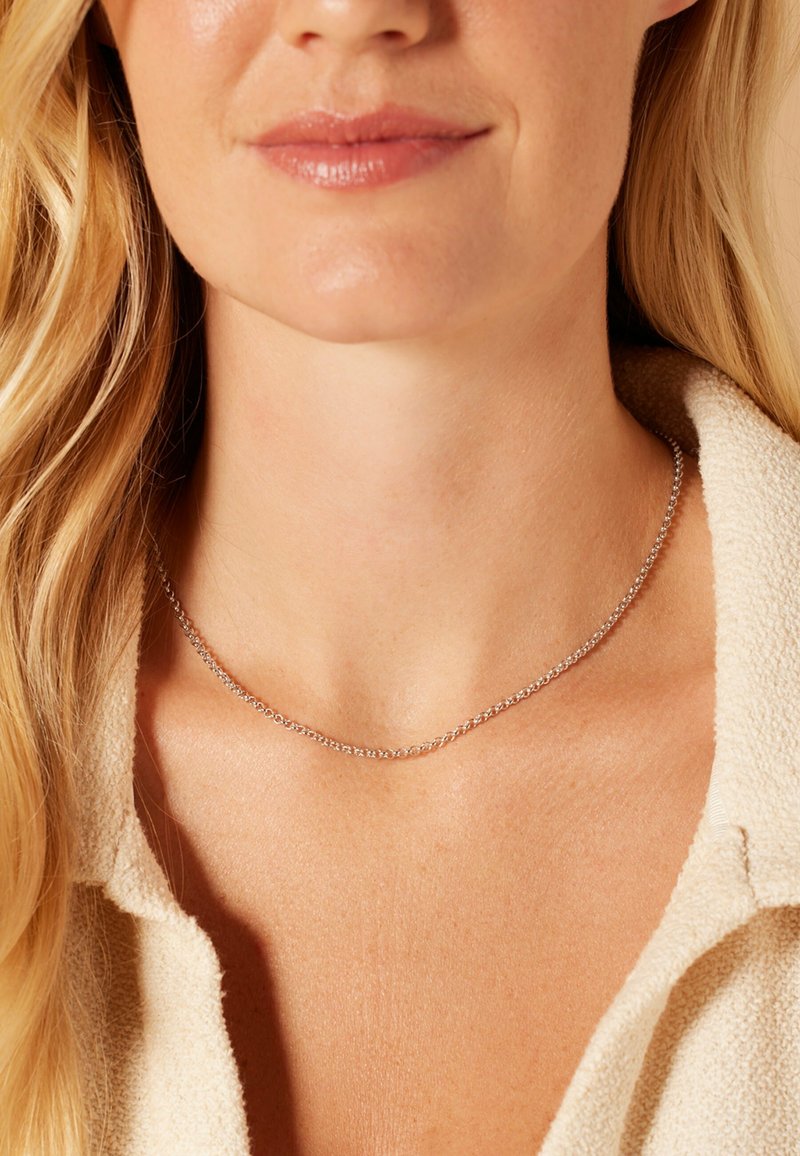 Collier en argent avec un design de chaîne délicate et fine. Porté autour du cou, mettant en valeur une texture lisse et un éclat subtil contre la peau.