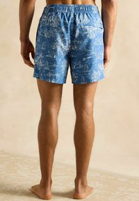 Pantaloni scurți de baie cu un model albastru, decorat cu imprimeuri de bărci cu pânze și palmieri, având un elastic la talie și un buzunar la spate.
