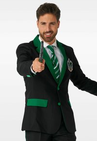Schwarze Anzugjacke mit grünen Akzenten, mit einem Wappen, passender gestreifter Krawatte und hält einen Zauberstab. Glatte Stoffstruktur.